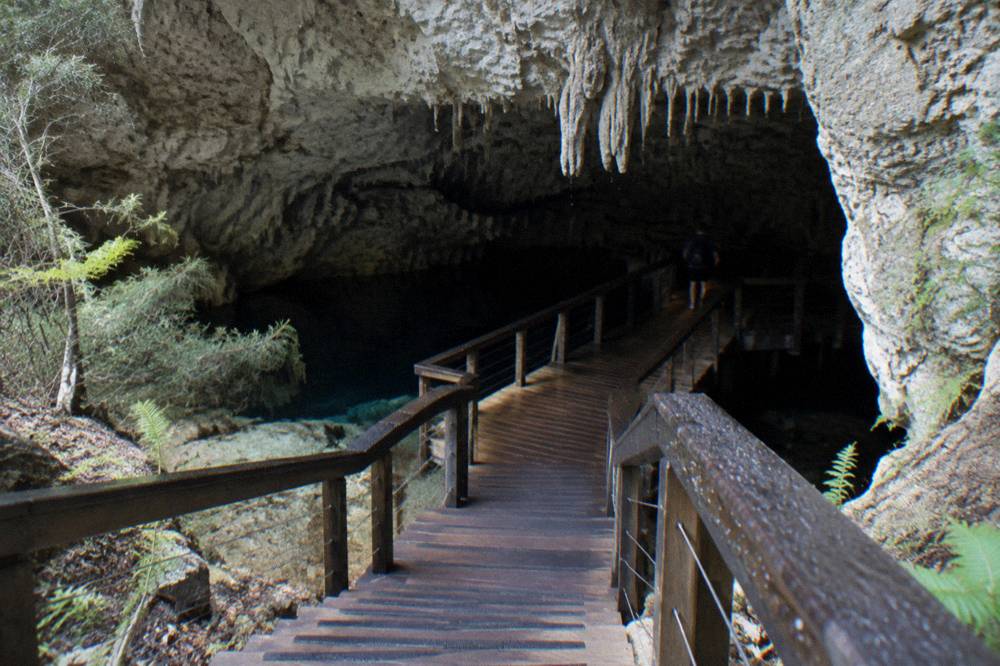 Wooden walkway leading into a dim limestone cave chamber with stalactite formations