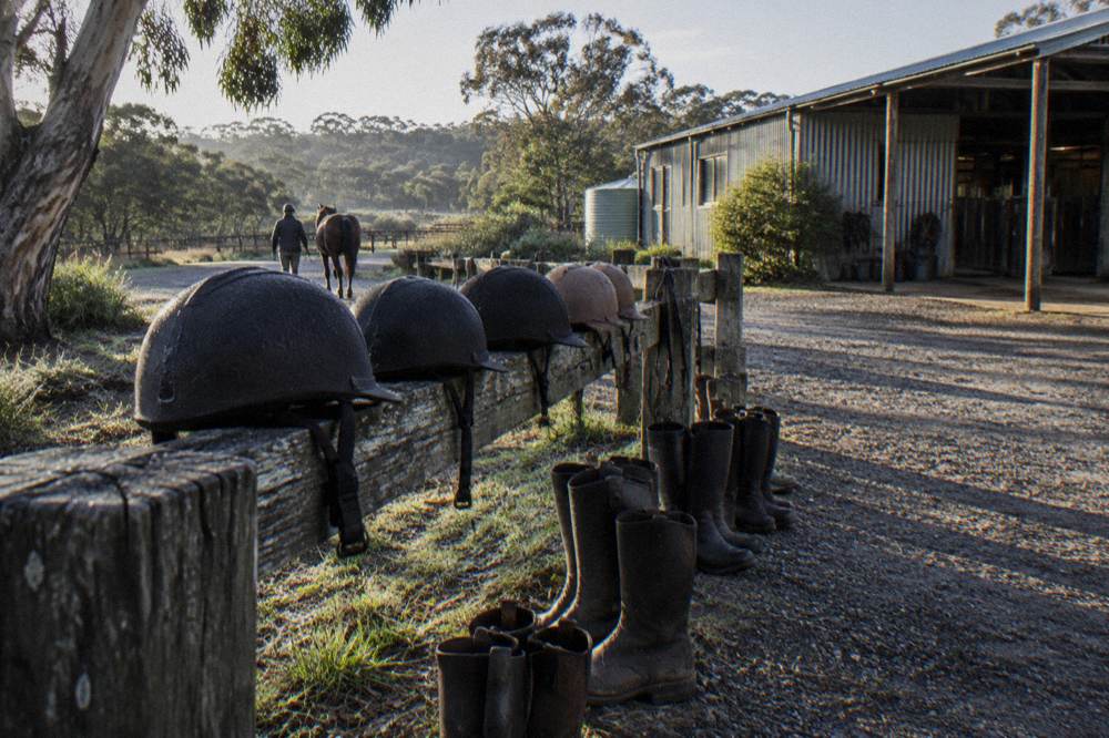 A row of riding helmets and boots set out on a fence rail at a farm yard before a trail ride