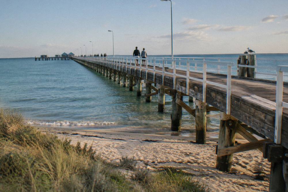 A wooden jetty stretching out over calm blue water beside a small coastal town