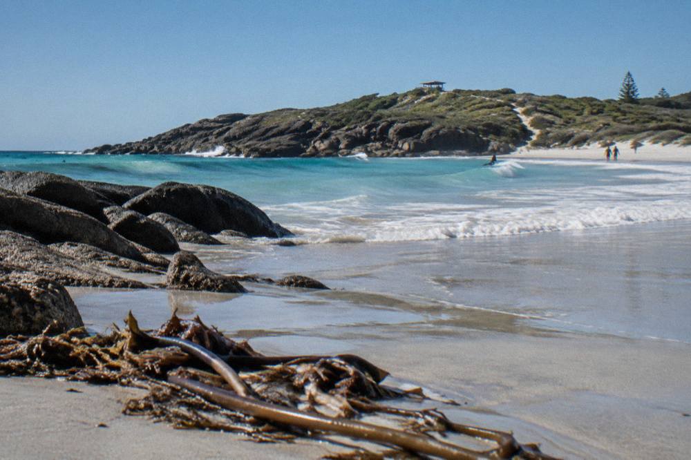 A sandy beach with turquoise water and a rocky headland under a clear sky