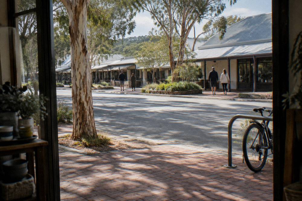 A country town street with shops and people strolling under trees