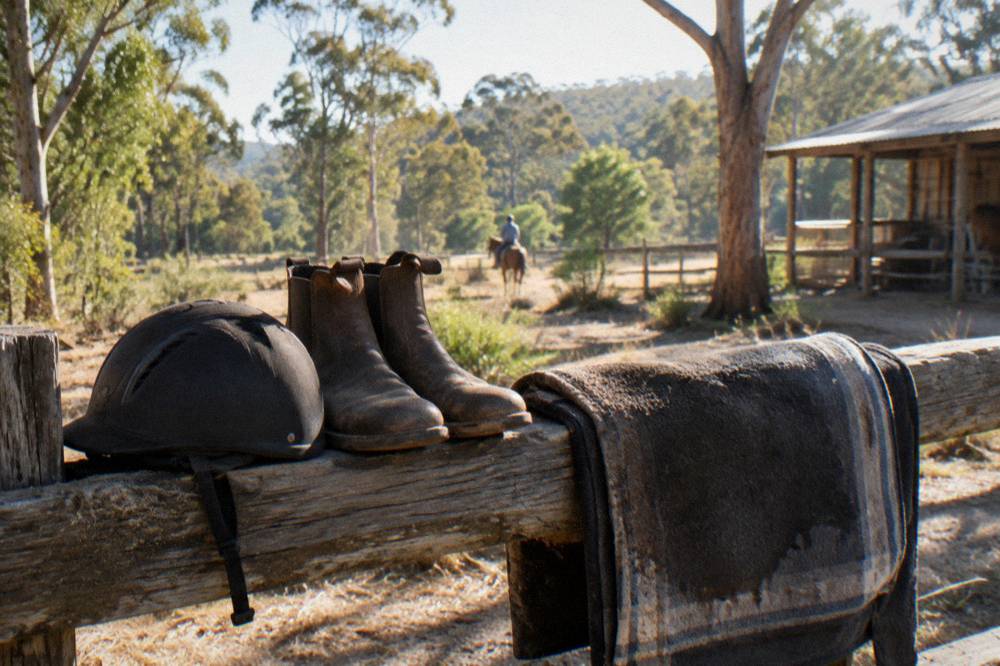 Riding helmet and boots resting on a fence rail