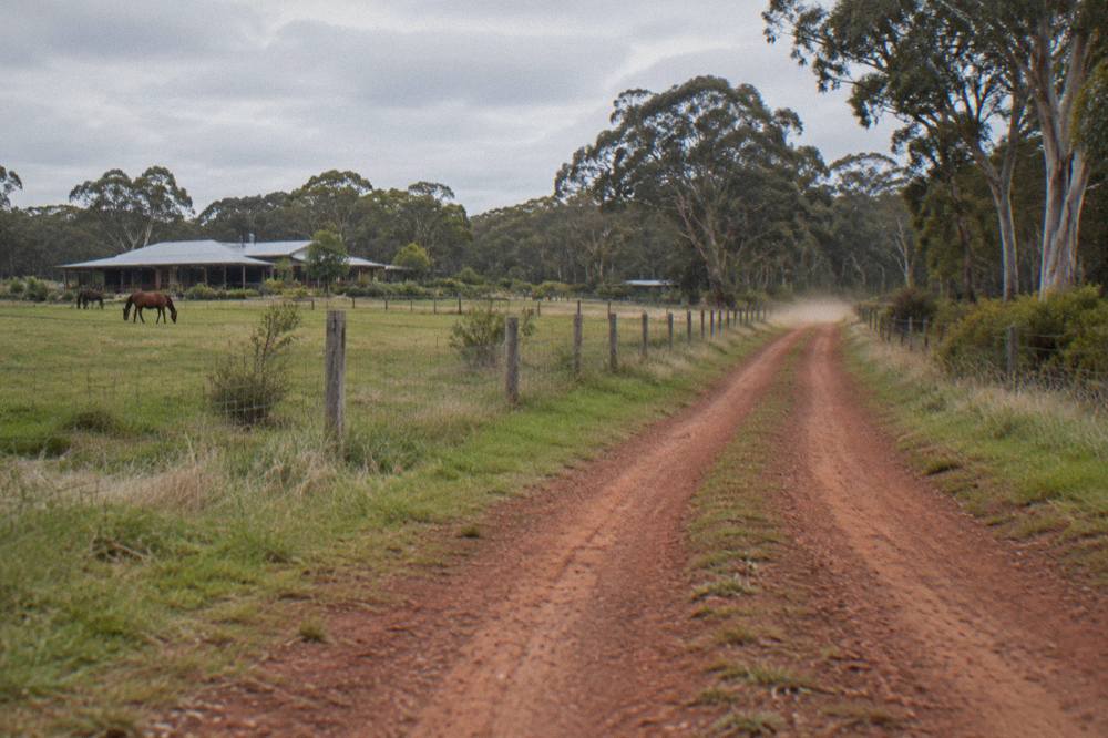 A gravel country road winding past farmland and tree lines near Margaret River