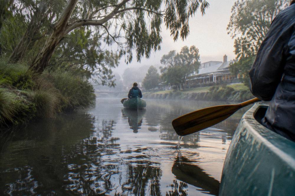 Canoes floating on calm river water between forested banks