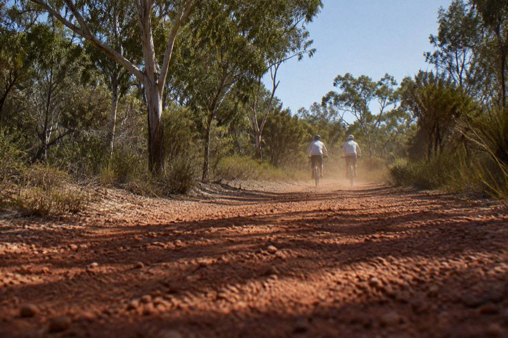 Riders in light long-sleeved shirts and helmets on a sunny bush trail